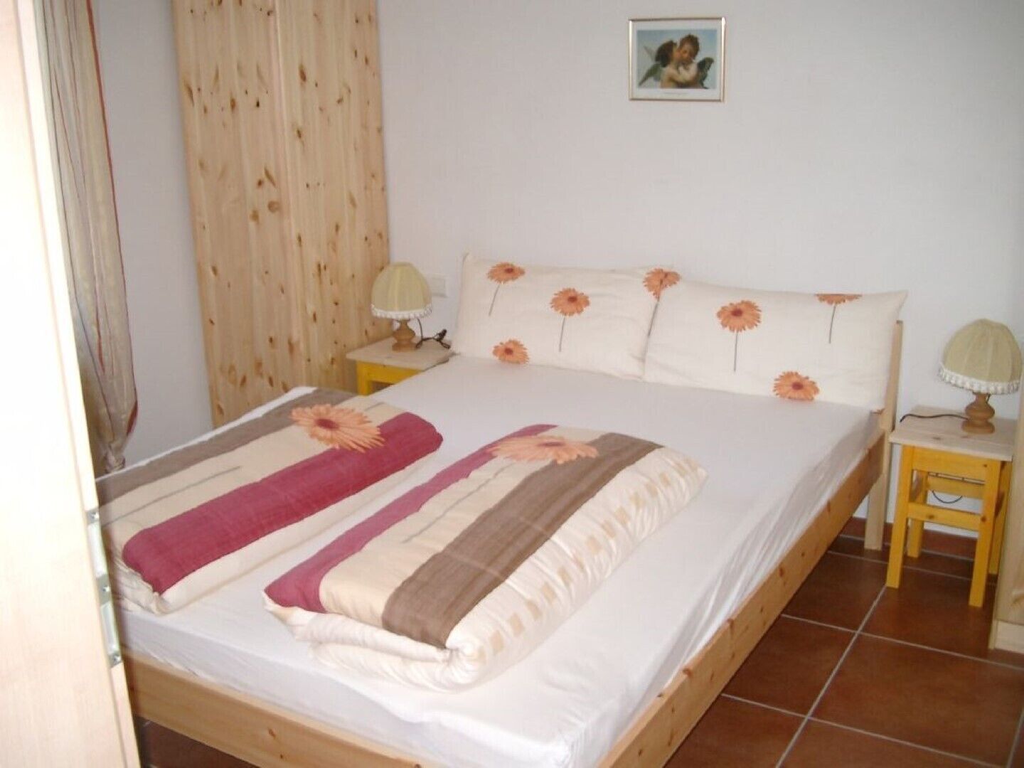 A double bed with a floral bedspread, two bedside lamps, and a framed picture on the wall.