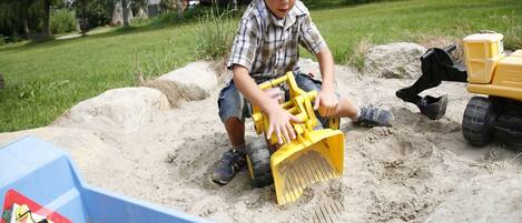 A child playing with sand and toy vehicles in an outdoor setting.
