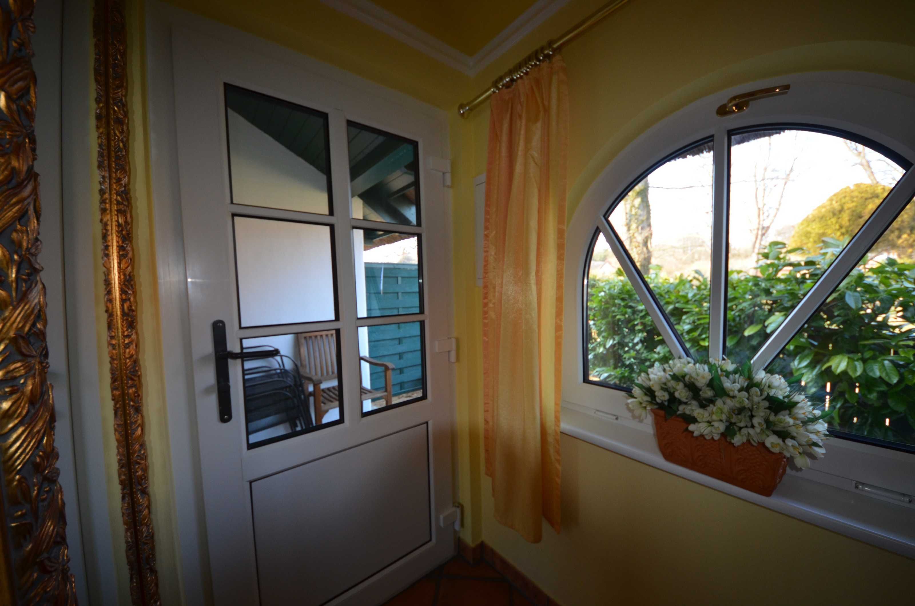 Uma porta com janela, cortina e um vaso de flores no parapeito.