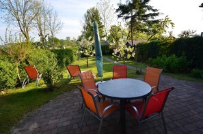 An outdoor patio with a round table and orange chairs, surrounded by greenery and trees. - 17g balaclava 5 persons behind - Reethäuser 17 / Fam. Kröning / TZR (Gager)