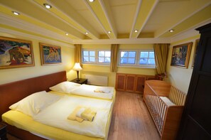 A hotel room with two beds, a crib, a window with curtains, and artwork on the walls. - 17g balaclava 5 persons behind - Reethäuser 17 / Fam. Kröning / TZR (Gager)
