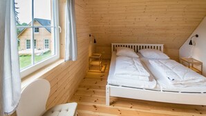 Une chambre avec un plancher en bois et un plafond en pente, un lit avec une literie blanche, une table de chevet, une chaise et une fenêtre avec des rideaux.