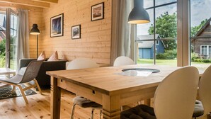L’intérieur est en bois et comprend une table à manger, des chaises et un canapé. Des tableaux encadrés ornent le mur, et une grande fenêtre offre une vue sur l’extérieur.