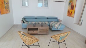 Ett vardagsrum med en blå soffa, två fåtöljer i rotting, ett soffbord i trä och konstverk på väggarna.