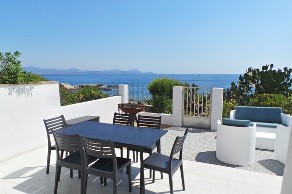 A terrace with a table and chairs, a fire pit, and a view of the sea.