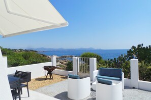 A terrace with outdoor seating, a barbecue, and a view of the sea and mountains.