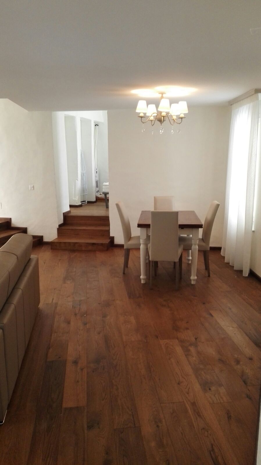 Un espace repas avec une table et des chaises en bois, un lustre et un escalier menant à une autre pièce.