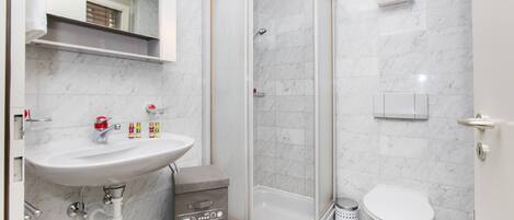 Un baño moderno con ducha de vidrio, lavamanos blanco y retrete.