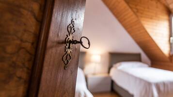 Eine Holztür mit einer verzierten Schlüsselloch, ein Bett und ein Nachttisch in einem Zimmer mit Holzbalkendecke.