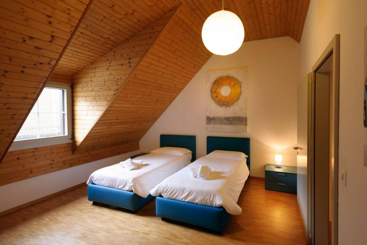 Un dormitorio con dos camas, vigas de madera en el techo, un tragaluz y una obra de arte en la pared.