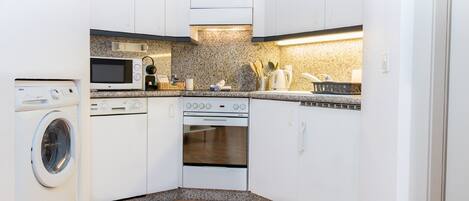 A compact kitchen with a washing machine, microwave, stove, and oven.