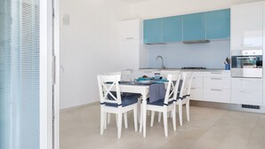 Una cocina moderna con armarios blancos, un muro azul de acento y un comedor con sillas blancas y una mesa dispuesta para cuatro.