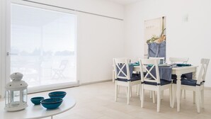 Un comedor con una mesa y sillas blancas, un ventanal con persianas y un cartel en la pared.