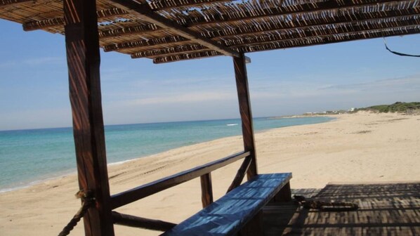 Blick auf einen Strand mit einer Holzkonstruktion, darunter eine Bank und ein Tisch.