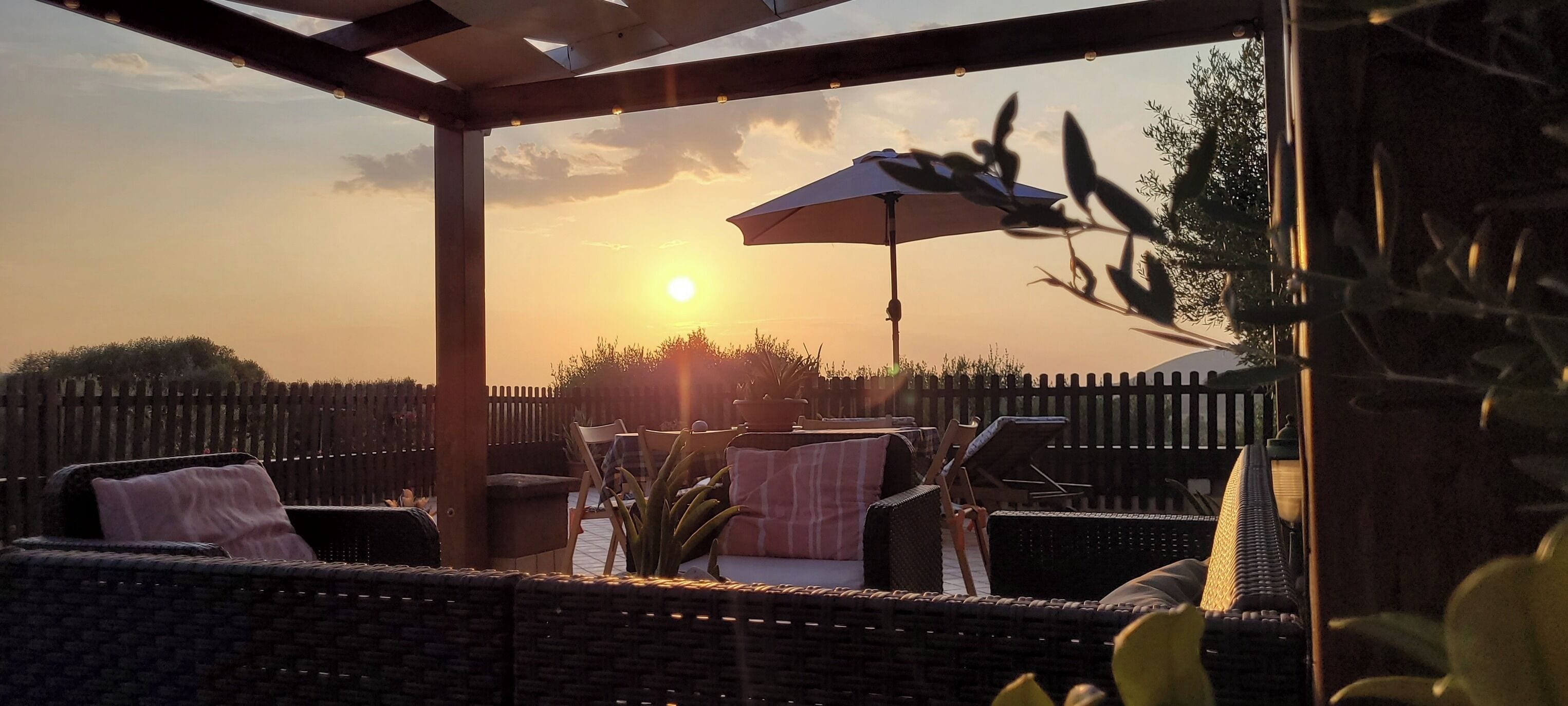 A patio area with wicker furniture, an umbrella, and a view of the sunset.