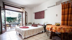 A bedroom with a bed, a dining table with a fruit bowl, a window with curtains, and a view of the outside. - Studioflat 1 - Residenza Su Prelau Residence - Sardinia South West Coast (Gonnesa)