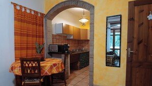A compact kitchen with a dining area, featuring a tiled floor, wooden cabinets, and a small table with a chair. - Studioflat 1 - Residenza Su Prelau Residence - Sardinia South West Coast (Gonnesa)