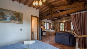 A room with a bed, a sofa, a painting, and a kitchen in the background.