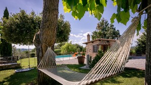 A hammock tied to a tree in a grassy area with a stone building and a swimming pool in the background.
