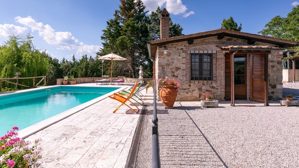 A stone building with a pool, outdoor seating, and potted plants.