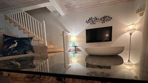 Ein modernes Wohnzimmer mit einem Glastisch, einer weißen Schale, einem Flachbildfernseher und einer Treppe mit Holzbalken.