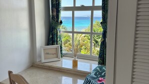 Ein Zimmer mit Blick auf einen Strand, ein Holzstuhl, ein kleiner Tisch und ein gerahmtes Bild auf dem Fensterbrett.