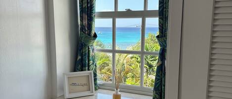 A room with a window overlooking a beach, a wooden chair, a small table, and a framed picture on the windowsill.