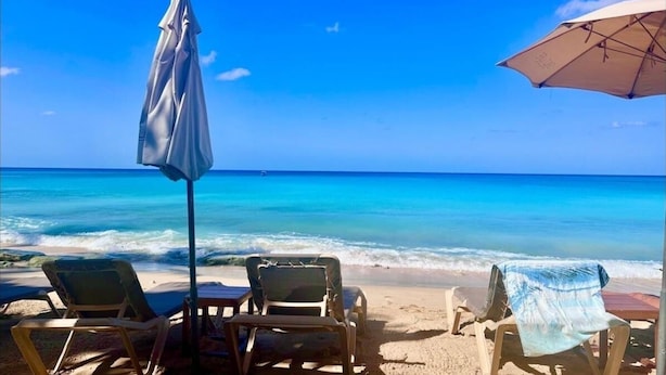 Ein Strand mit zwei Liegestühlen, einem Tisch, einem Sonnenschirm und Blick auf das Meer.
