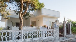 A modern two-story house with a white exterior, a stone base, and a decorative white fence. - Salento Villa Emma - Green Apartment with Garden (Porto Cesareo)
