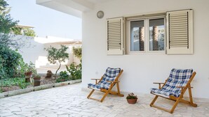 A patio with two wooden lounge chairs, a white wall, and a window with shutters. - Salento Villa Emma - Green Apartment with Garden (Porto Cesareo)