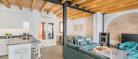 A modern kitchen with white cabinets, a bar stool area, a sofa, and a stone fireplace.