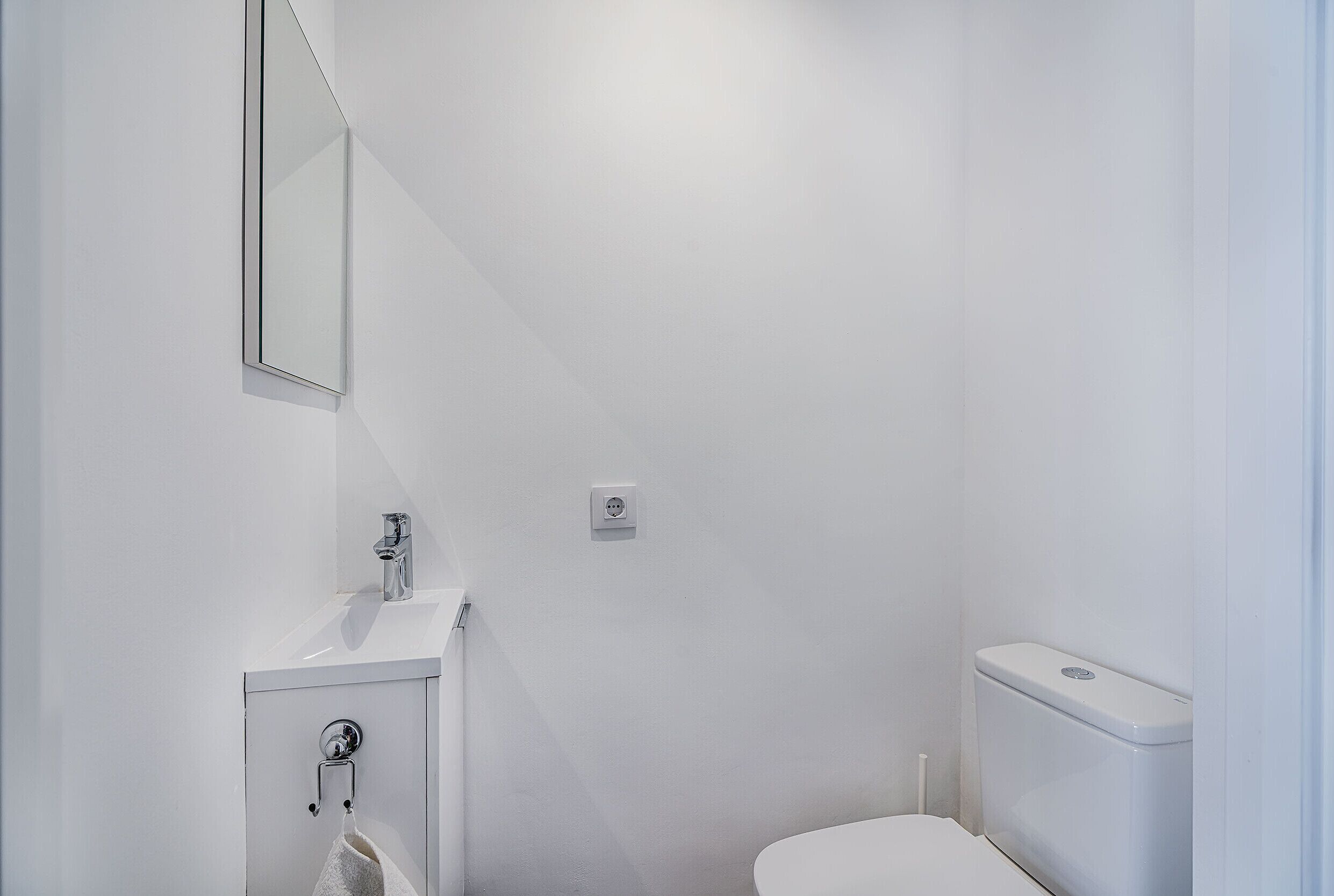 A small, white bathroom with a toilet, sink, and mirror.