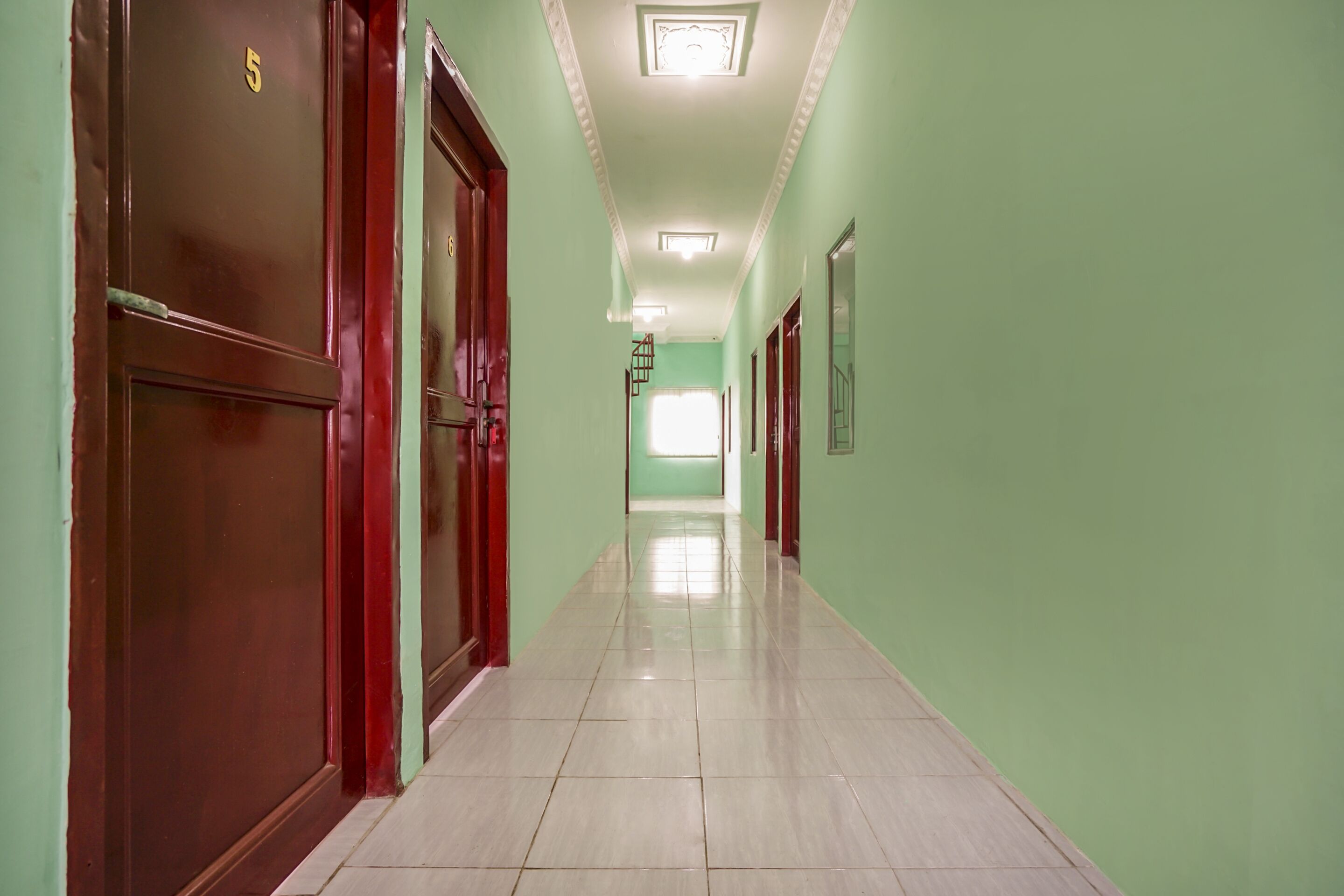 Un long couloir étroit aux murs verts et au sol carrelé.
