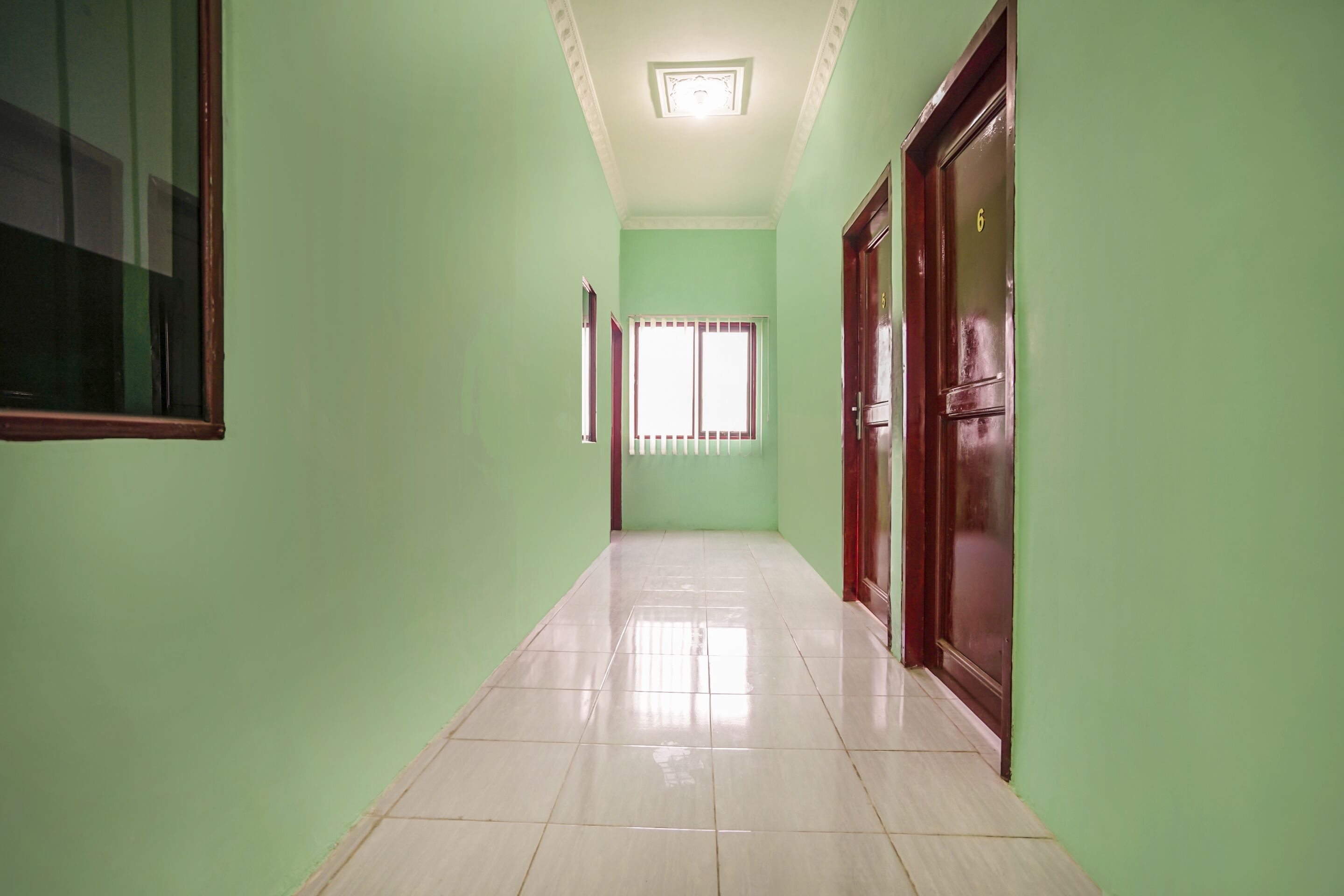 A hallway with green walls, a tiled floor, and a door with a number 6 on it.