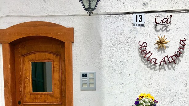Una porta de fusta amb una finestra, un rètol fixat a la paret i dues composicions florals sobre troncs de fusta.