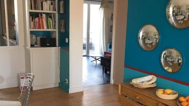 Un soggiorno con un divano blu, un tavolo da pranzo in legno con frutta e una libreria.