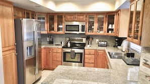 A modern kitchen with wooden cabinets, stainless steel appliances, granite countertops, and a built-in oven.