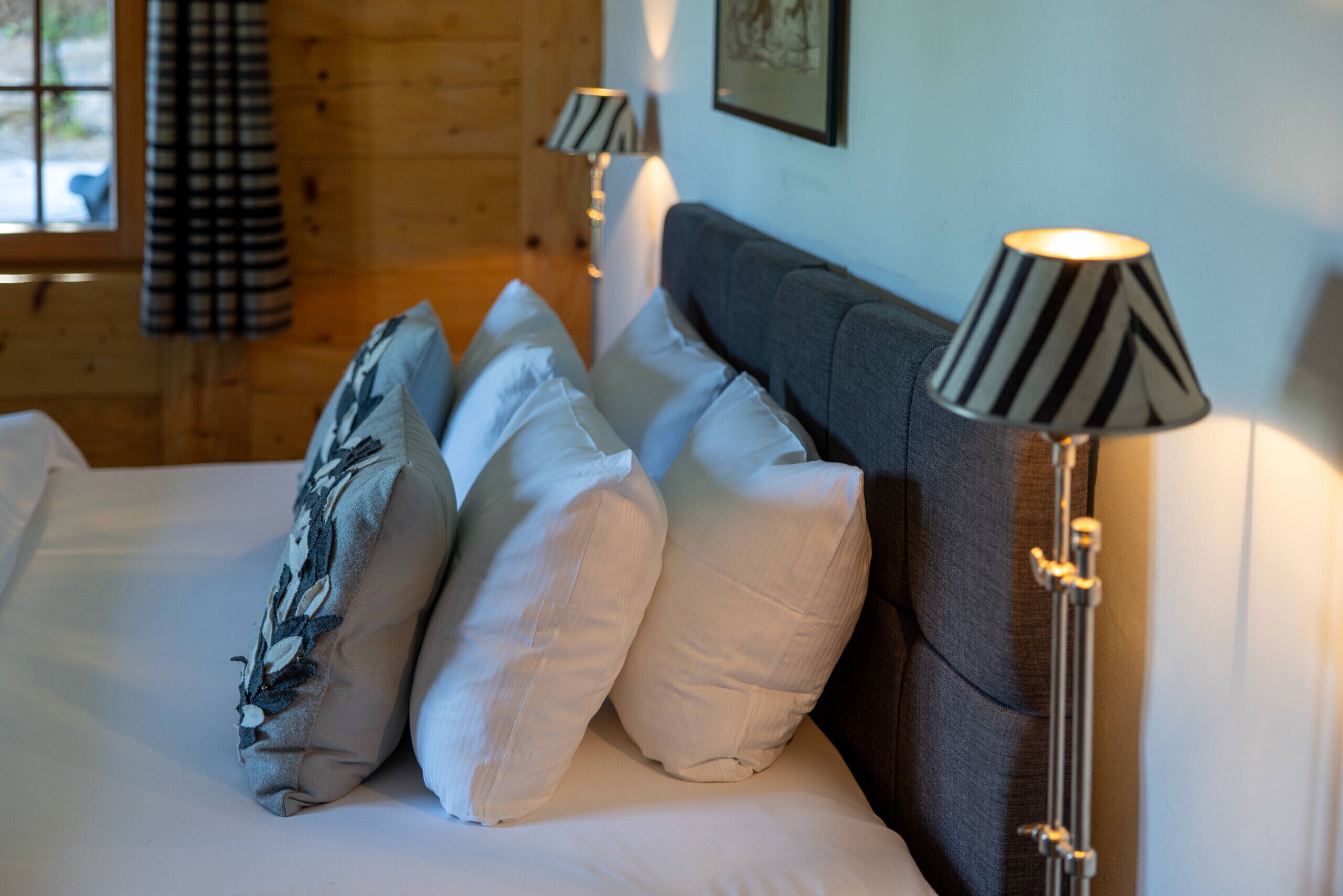 A bed with white linens, a grey headboard, and two lamps with striped lampshades.