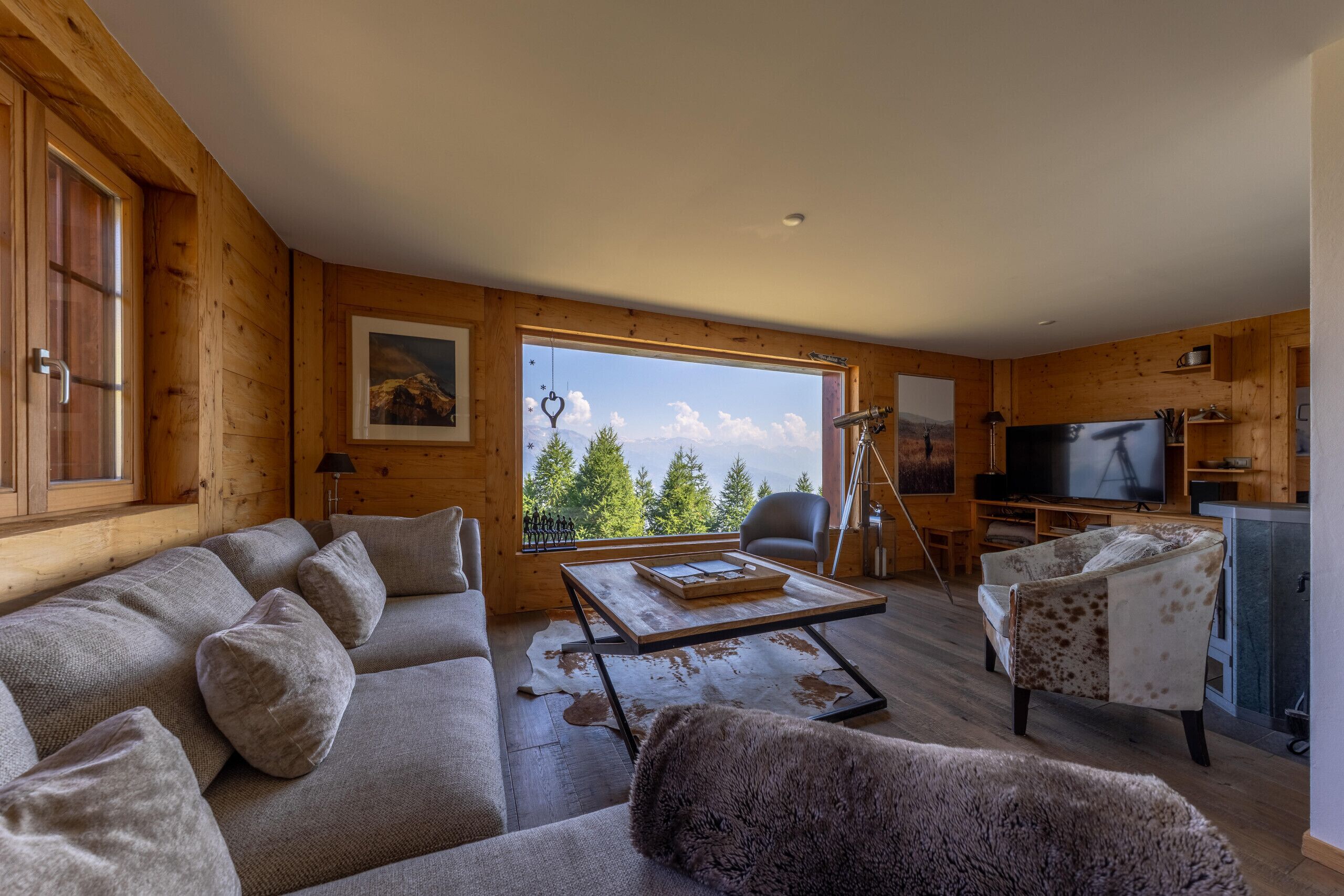 A wooden interior with a sofa, armchair, TV, and a view of trees through a window.