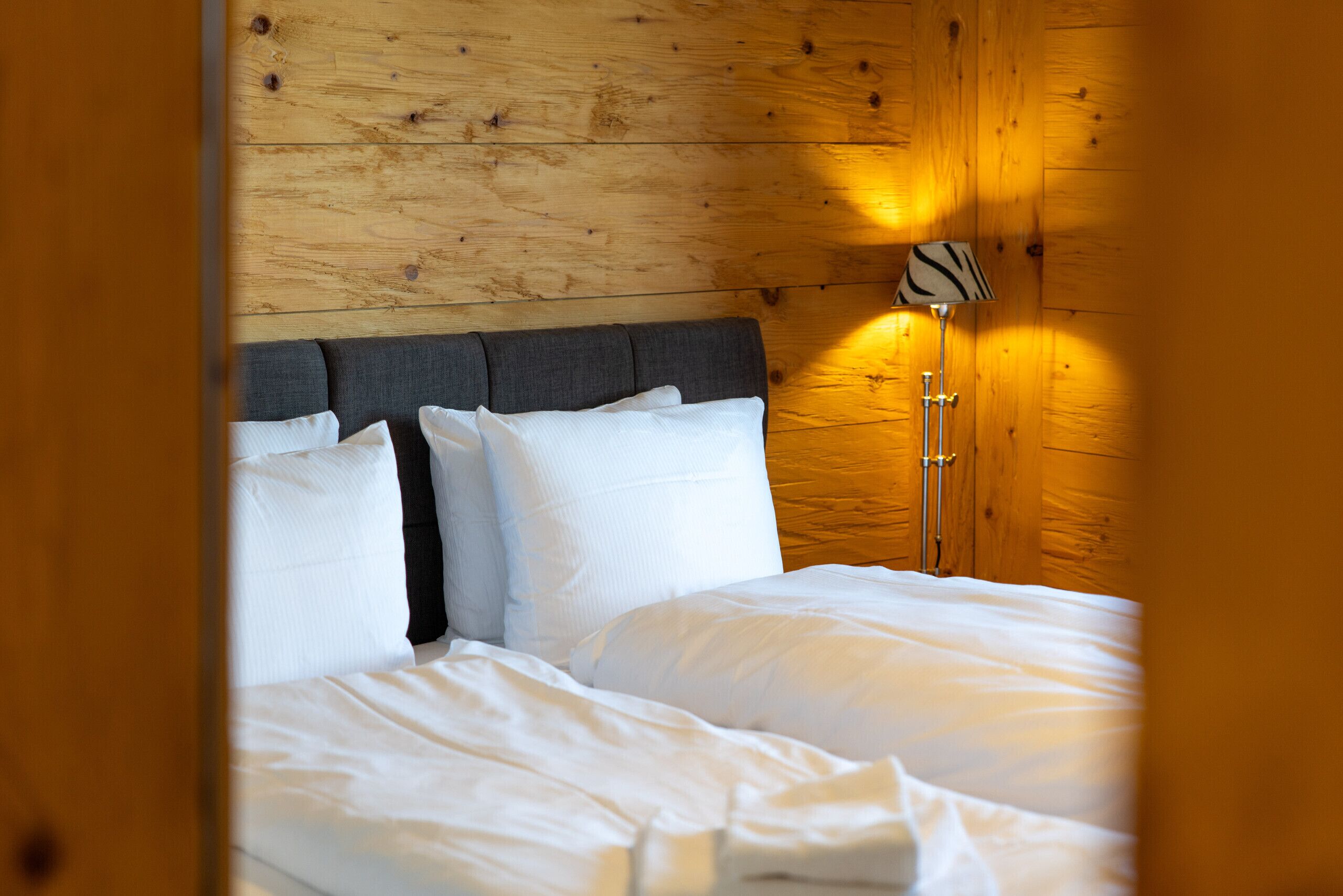 A bed with white linens, a grey headboard, and a lamp with a zebra pattern on the wall.