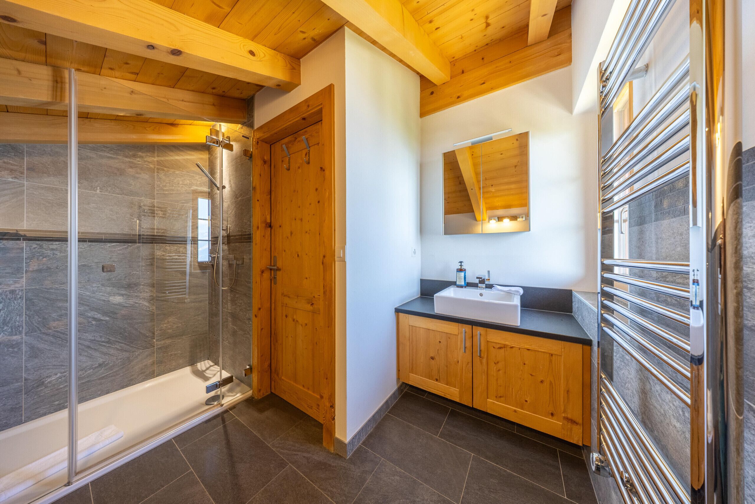 A bathroom with a glass shower enclosure, wooden cabinets, a sink, and a mirror.