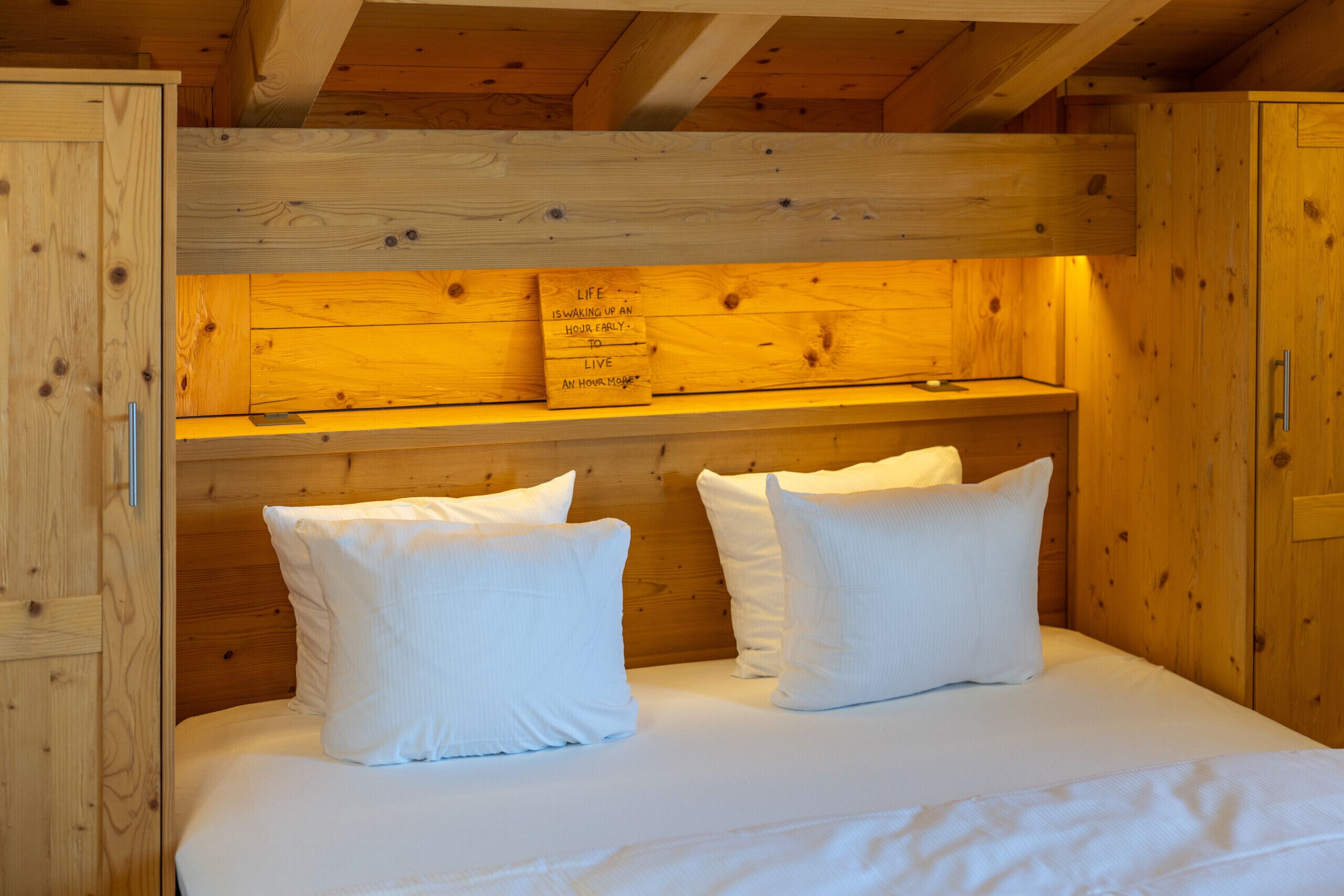 A wooden cabin-style room with a bed, pillows, and a shelf with a motivational quote.