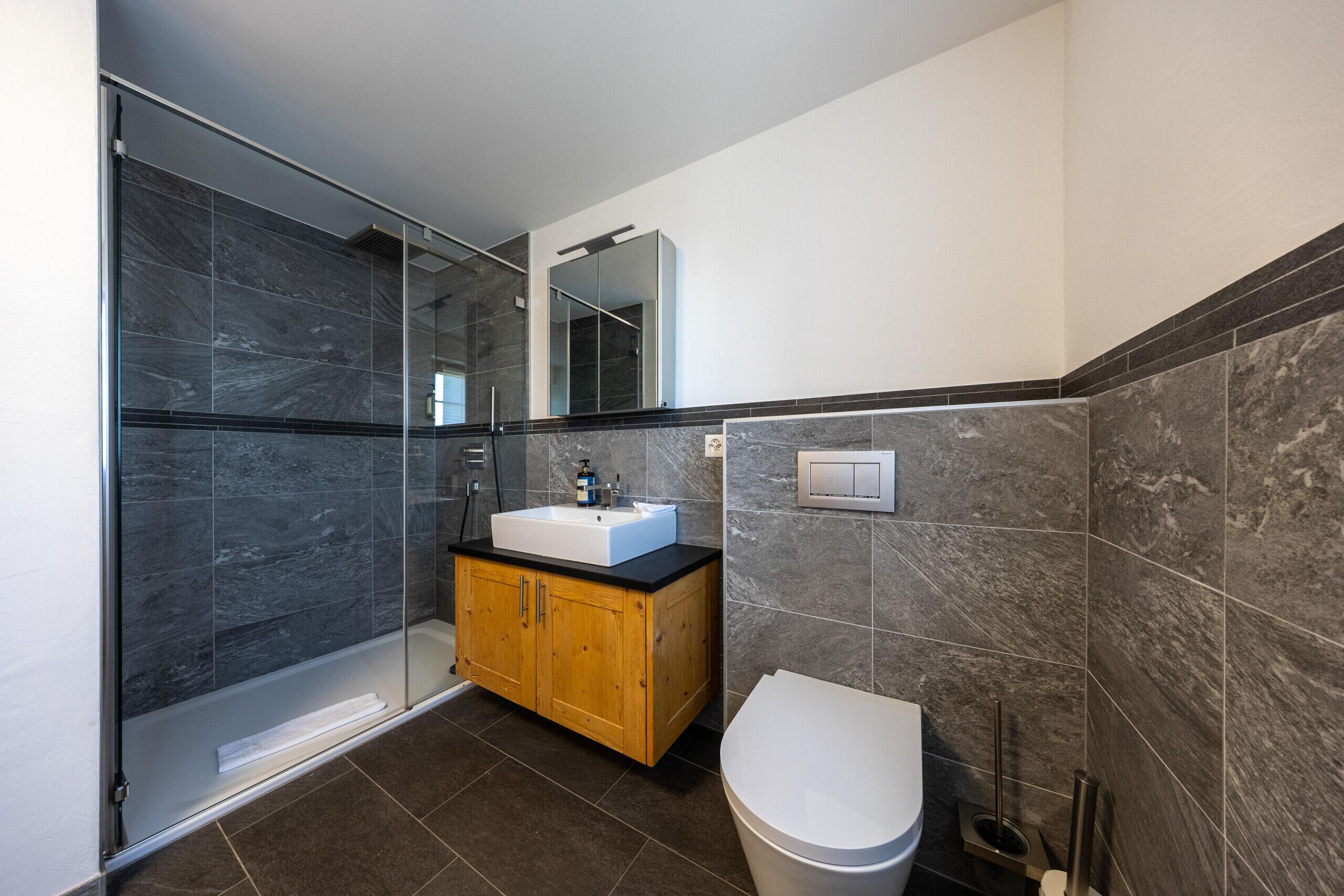 Een moderne badkamer met een douchecabine van glas, een houten wastafelmeubel en een wit toilet.