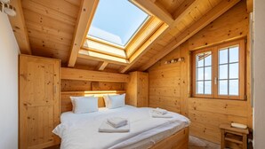 A wooden cabin bedroom with a skylight, a bed with white linens, and a window with a view. - Chalet Riquet - ski-in/out - luxe (Haute-Nendaz)