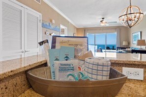 A kitchen counter with a bowl containing various items, a ceiling fan, and a view of the ocean through large windows.