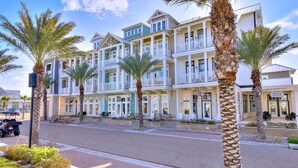 Un hôtel situé en bord de mer, doté de nombreux balcons, de palmiers et d’une promenade qui longe la plage.