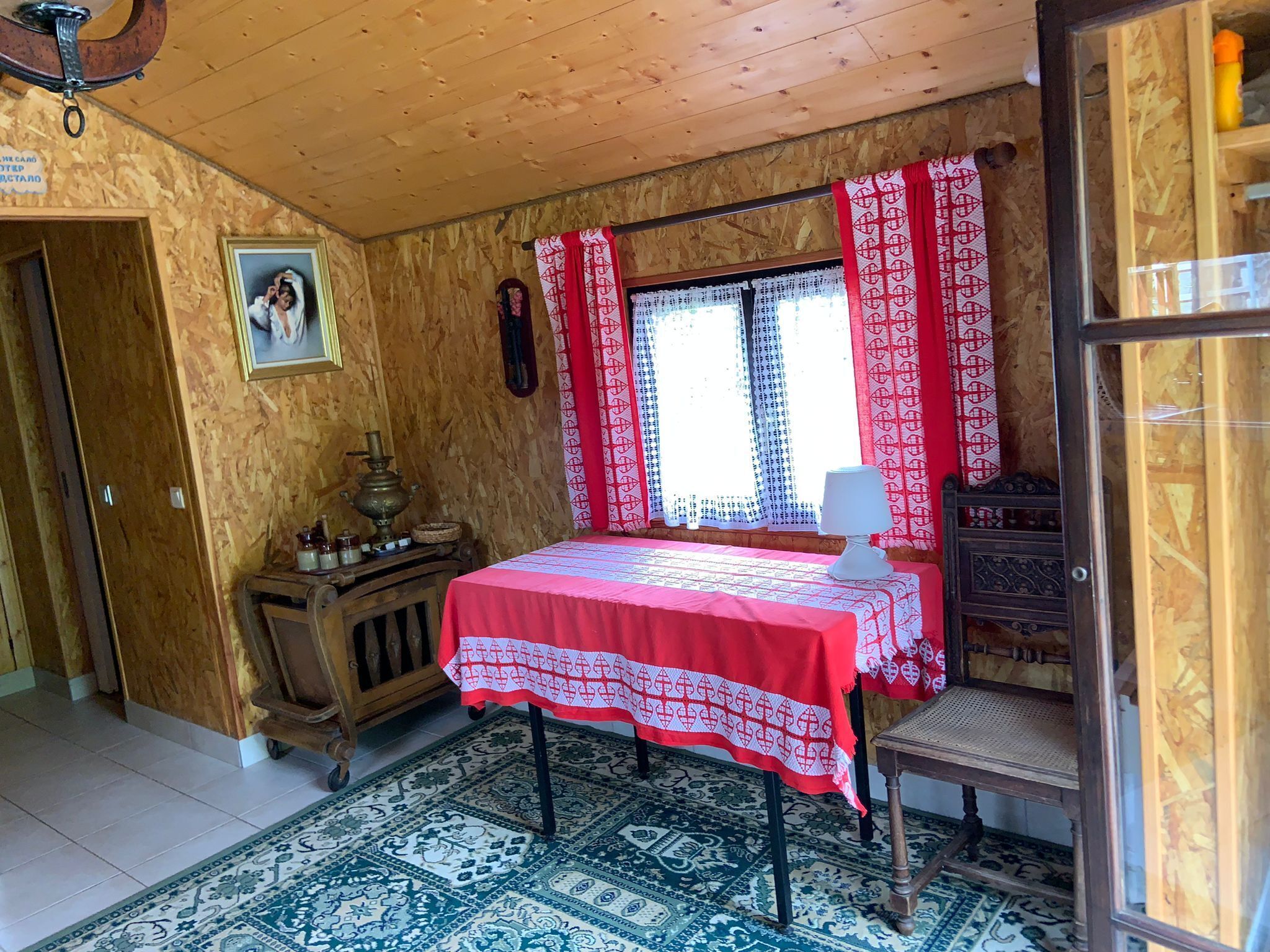 Une pièce avec un plafond en bois, un lit recouvert d’une couette rouge et blanche, une fenêtre avec des rideaux rouges, une armoire en bois et un tapis à motifs.