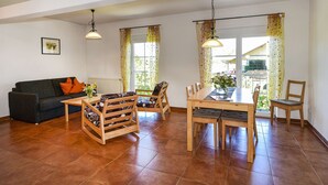 A living room with a sofa, wooden chairs, a dining table, and a window with curtains. - An oasis for parents, a paradise for children (Tettnang)