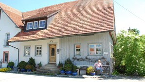 A two-story house with a red-tiled roof, a front porch with potted plants, and a small garden area. - An oasis for parents, a paradise for children (Tettnang)