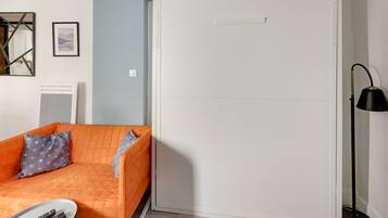 Ein Zimmer mit einem weißen Kleiderschrank, einem Bett mit orangefarbener Bettdecke, einer schwarzen Stehlampe und einer weißen Heizung.